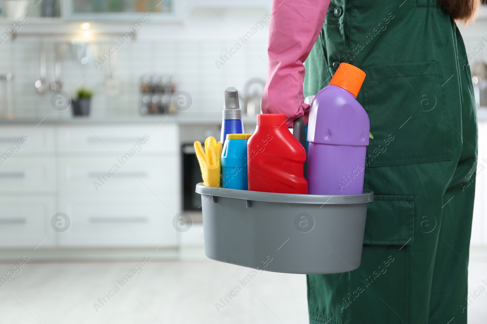 Photo of Worker in uniform with basin of detergents in kitchen, closeup. Cleaning service