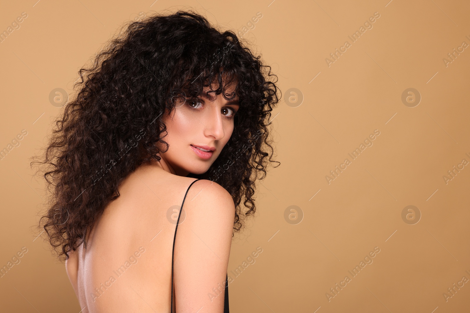 Photo of Beautiful young woman with long curly hair on beige background. Space for text