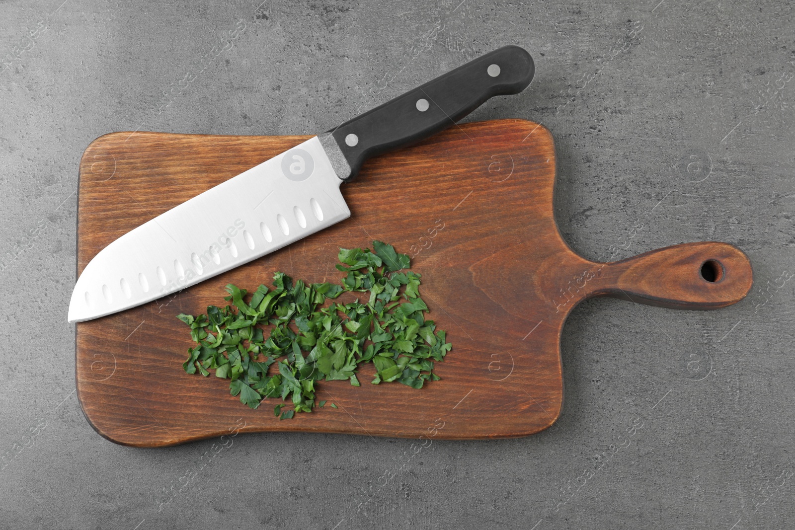Photo of Wooden board with sharp knife and chopped parsley on grey background, top view