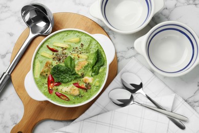 Photo of Saucepan with delicious green curry chicken soup and kitchenware on white marble table, flat lay