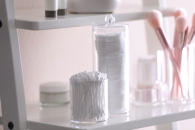 Photo of Cotton buds and pads in transparent holders on shelf