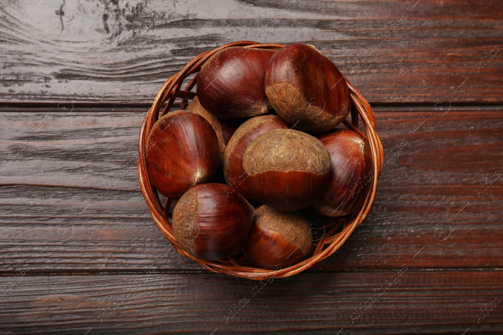 Photo of Sweet fresh edible chestnuts in wicker bowl on wooden table, top view