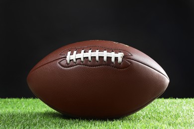 Photo of Leather American football ball on green grass against black background, closeup