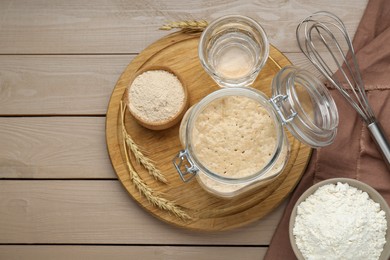 Photo of Leaven, ears of wheat, whisk, water and flour on beige wooden table, flat lay