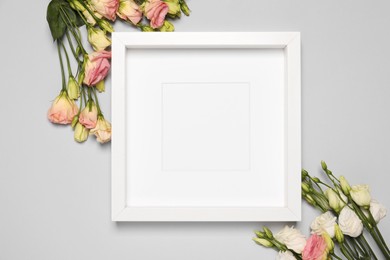 Photo of Empty photo frame and beautiful flowers on light gray background, flat lay. Mockup for design