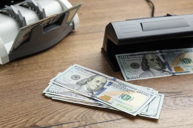 Photo of Modern currency detector with dollar banknotes on wooden table. Money examination device