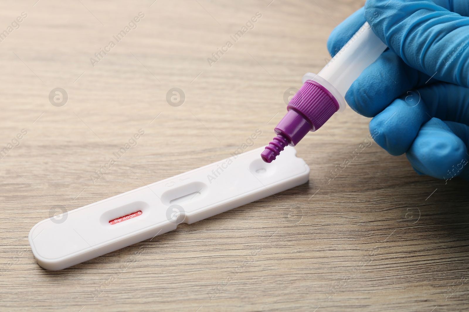 Photo of Doctor dropping buffer solution onto Covid-19 express test cassette at wooden table, closeup