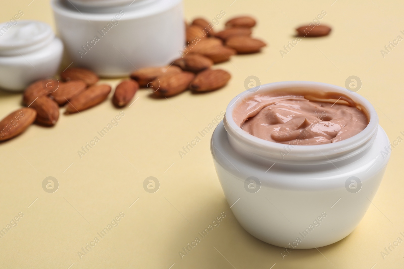 Photo of Jar of body cream and almond nuts on beige background
