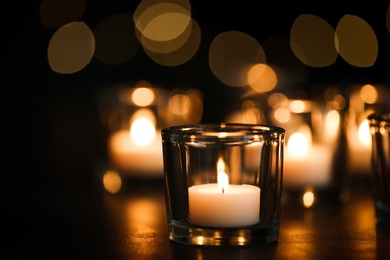 Burning candle on table against blurred background. Funeral symbol