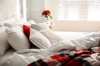 Photo of Cozy bed with red woolen blanket and cushions in room. Christmas interior design
