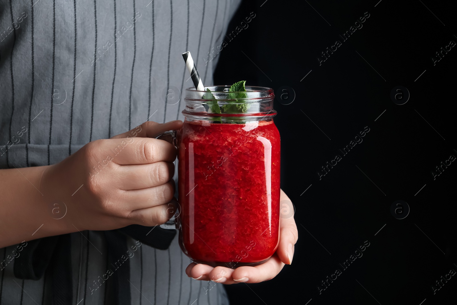 Photo of Woman holding tasty strawberry smoothie with mint on black background, closeup