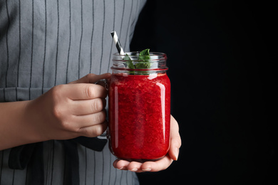 Woman holding tasty strawberry smoothie with mint on black background, closeup