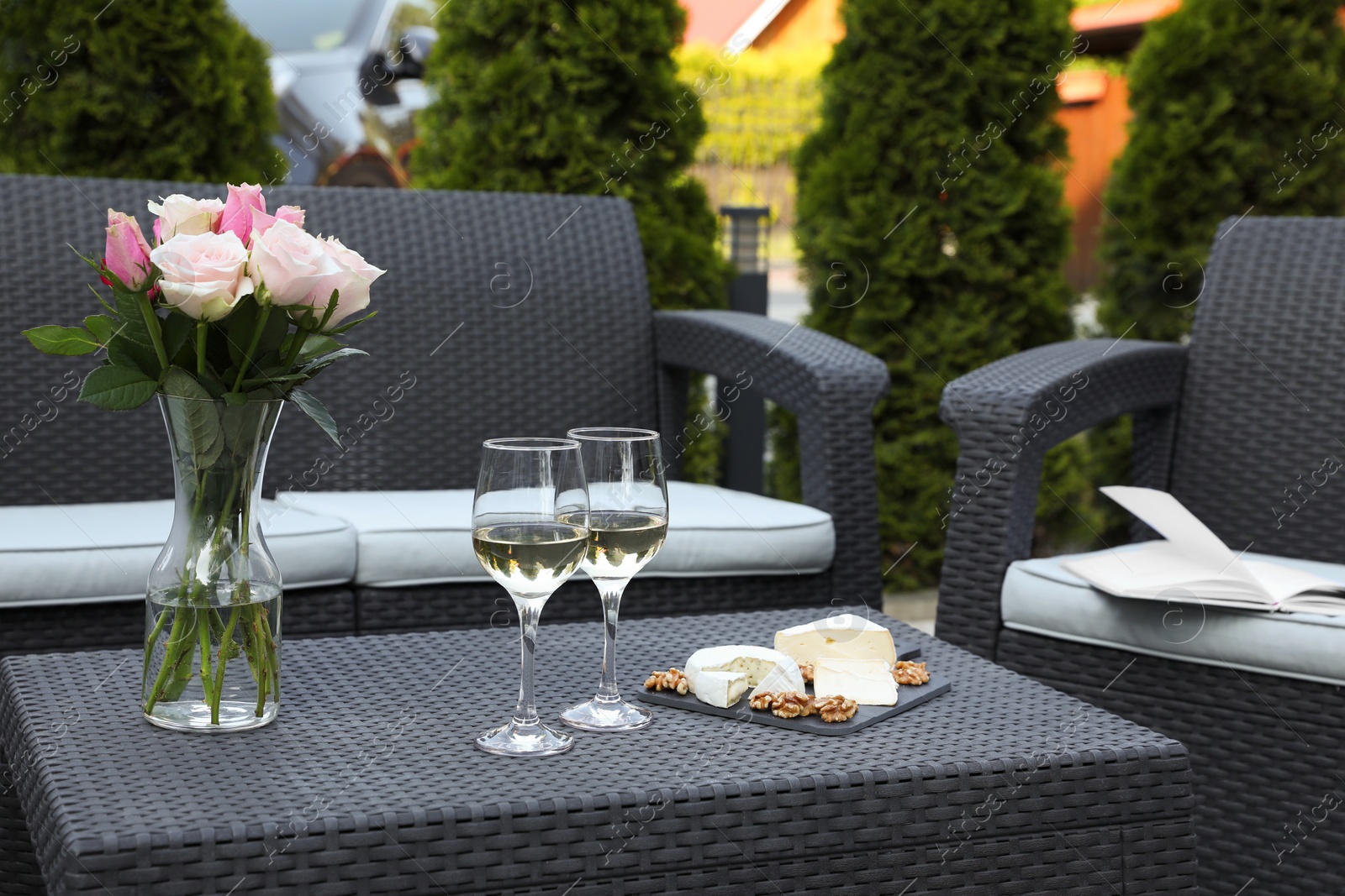 Photo of Vase with roses, glasses of wine and food on rattan table on outdoor terrace