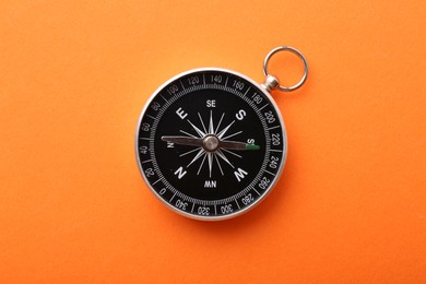 Photo of One compass on orange background, top view. Tourist equipment