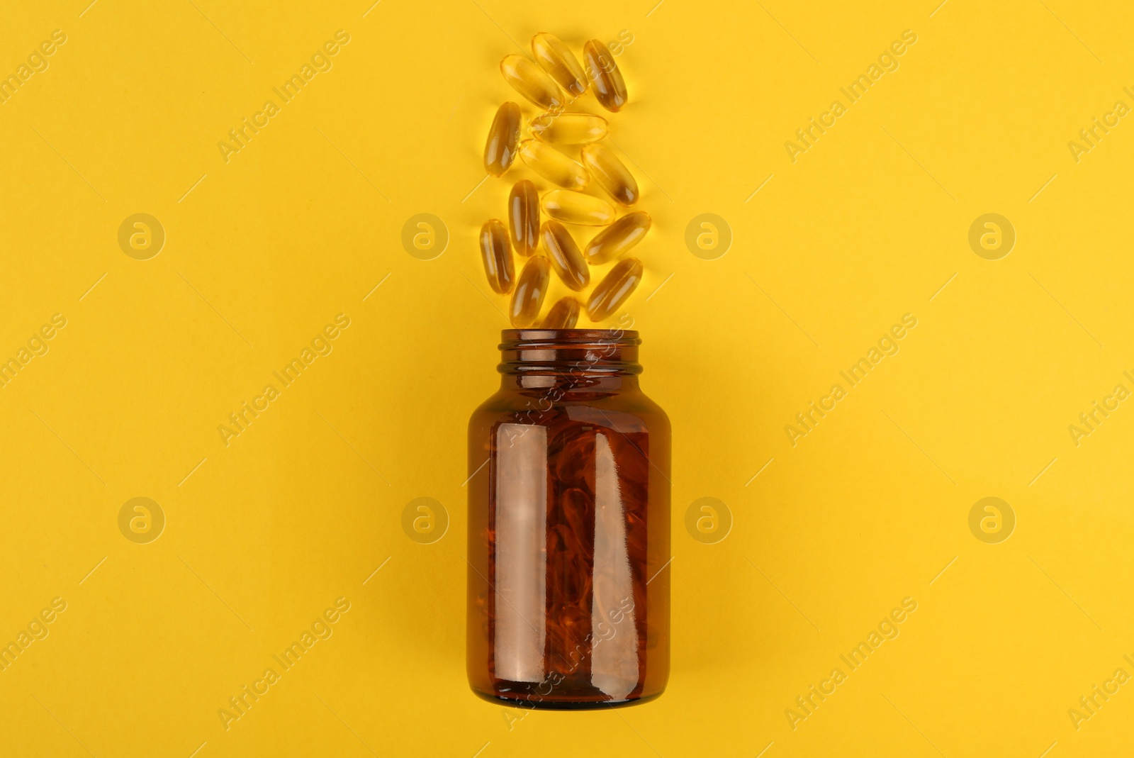 Photo of Glass medical bottle and vitamin capsules on yellow background, top view