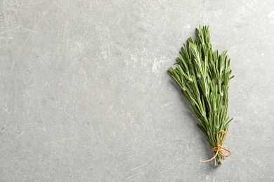 Photo of Fresh rosemary twigs tied with twine on gray table, top view