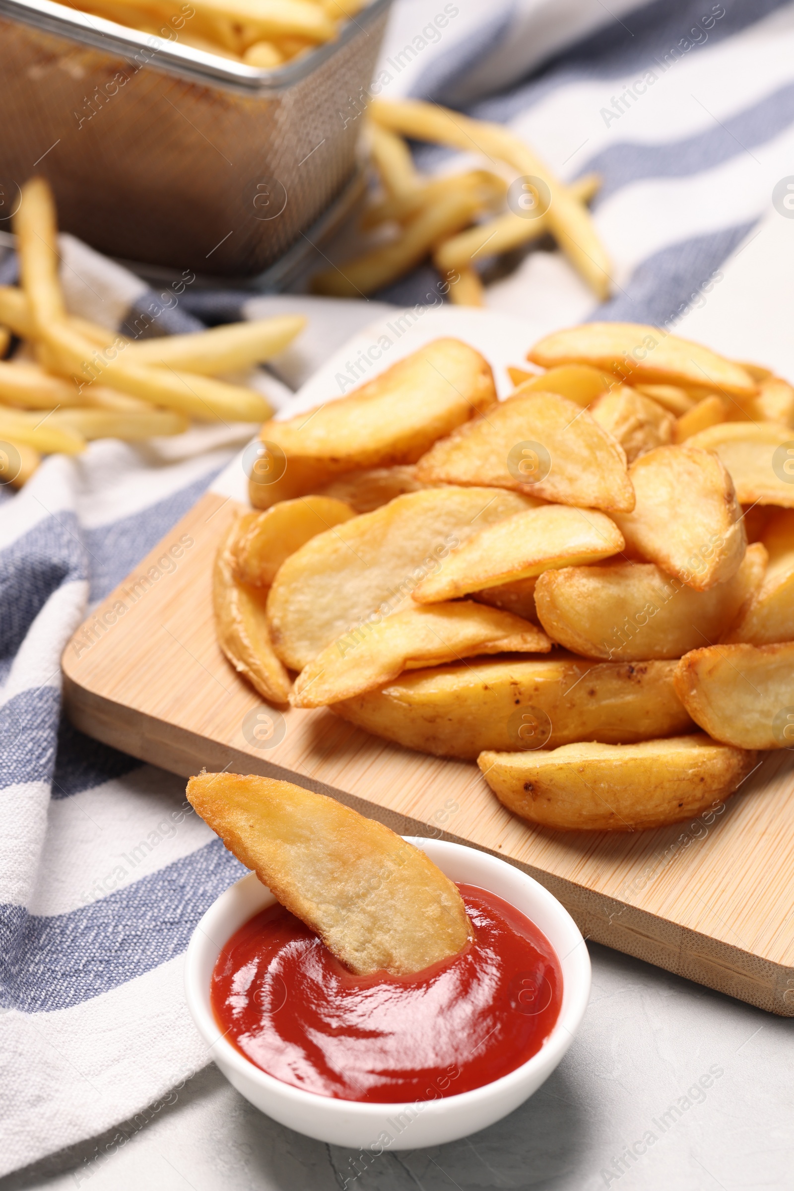 Photo of Delicious baked potato wedges and ketchup in bowl on light gray table, closeup