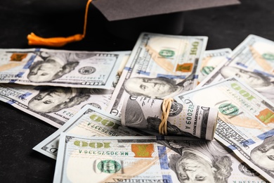 Photo of Dollar banknotes and student graduation hat on black background. Tuition fees concept