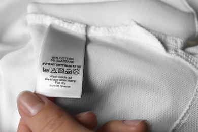 Photo of Woman reading clothing label with care symbols and material content on white shirt, closeup