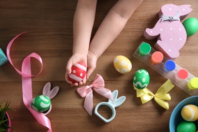 Photo of Little child holding painted Easter egg on wooden background, top view