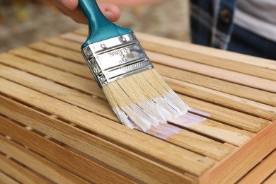 Photo of Man applying varnish onto wooden crate, closeup