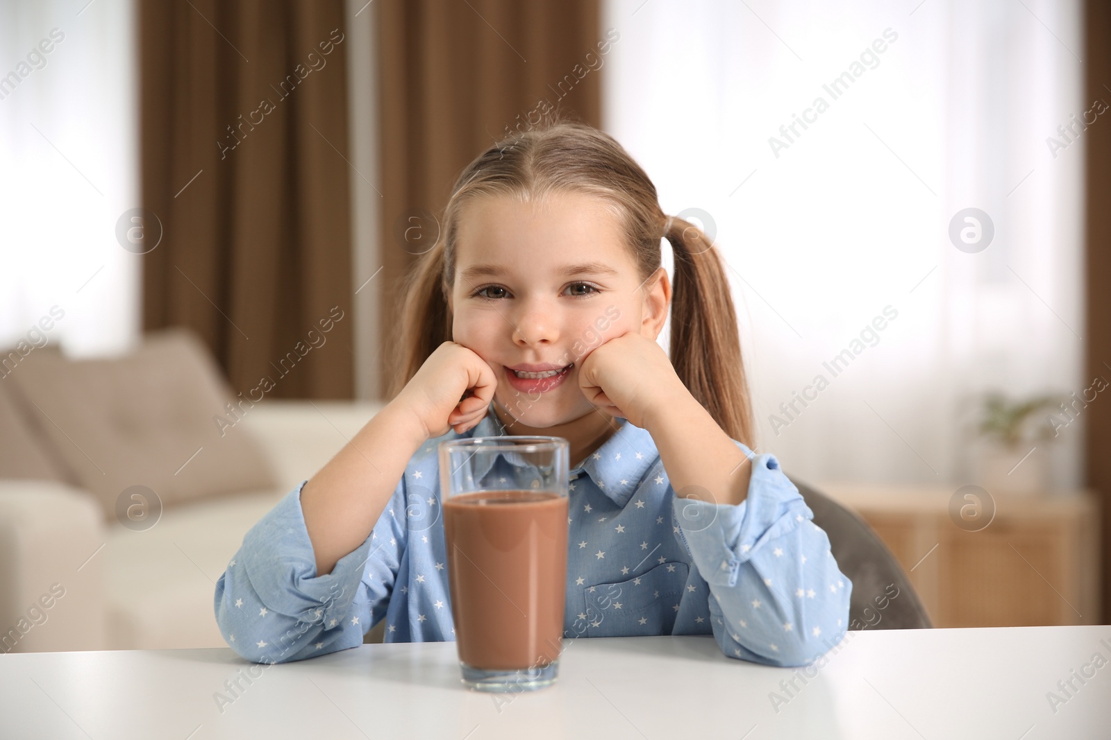 Photo of Cute little child with glass of tasty chocolate milk at home