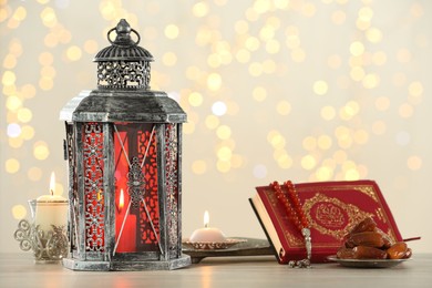 Photo of Arabic lantern, Quran, misbaha, candles and dates on table against blurred lights