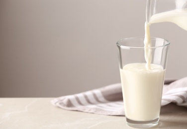 Photo of Pouring milk into glass on table against grey background. Space for text