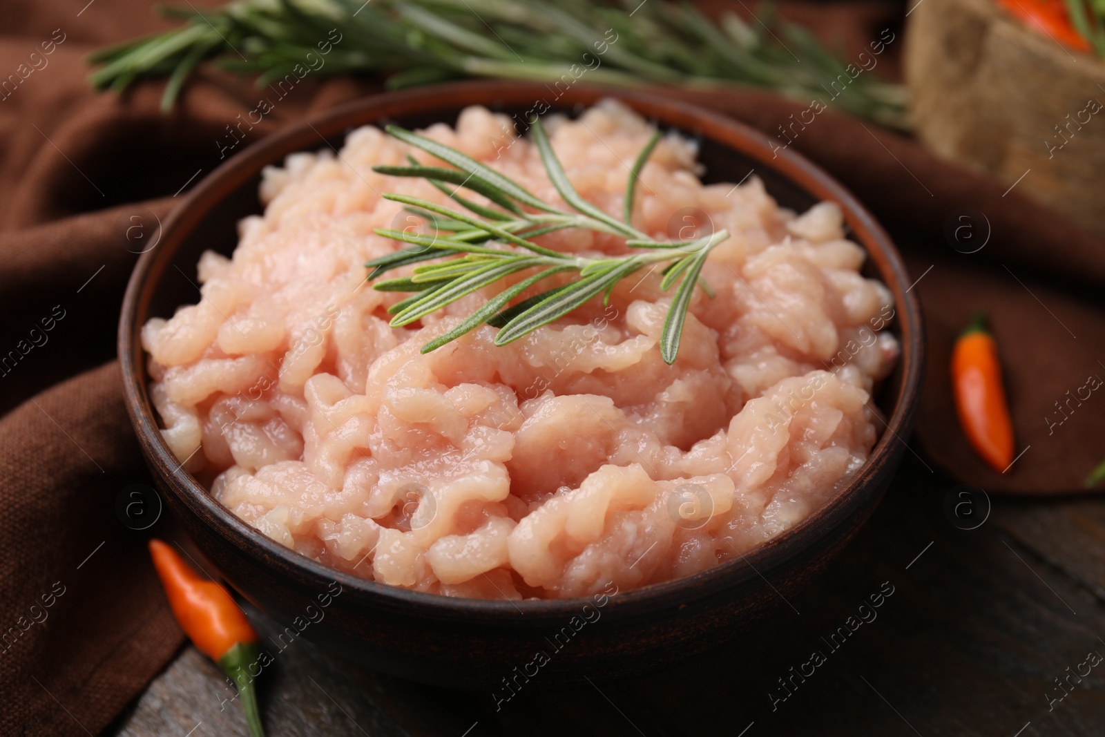 Photo of Fresh raw minced meat and rosemary in bowl on wooden table, closeup