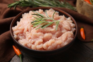 Photo of Fresh raw minced meat and rosemary in bowl on wooden table, closeup