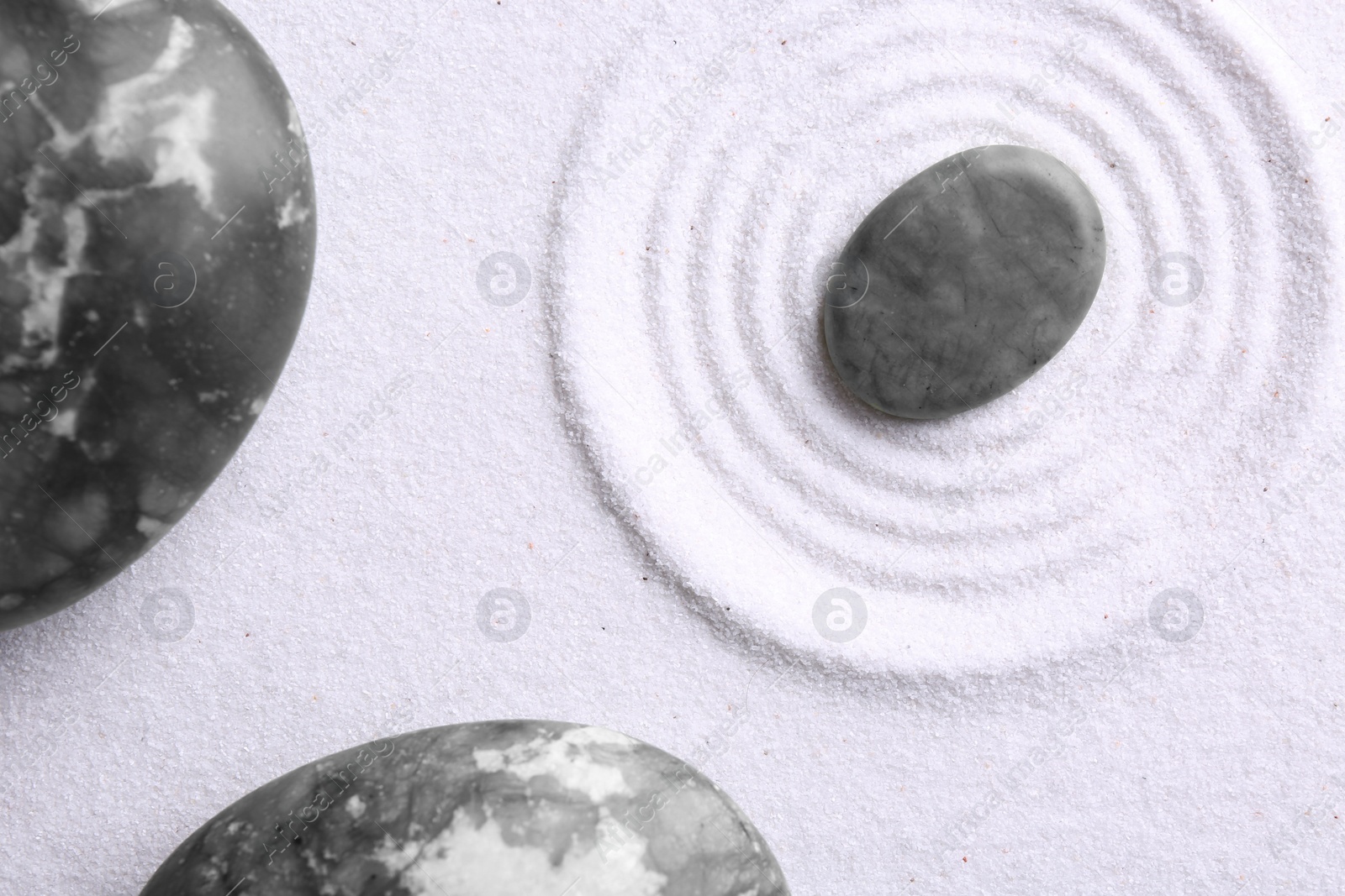 Photo of Zen garden stones on white sand with pattern, flat lay