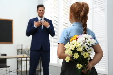 Photo of Schoolgirl with bouquet congratulating her pedagogue in classroom. Teacher's day