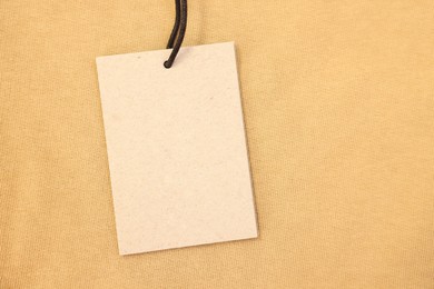 Photo of Cardboard tag on beige garment, top view. Space for text