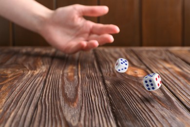 Image of Woman throwing white dice on wooden table, closeup