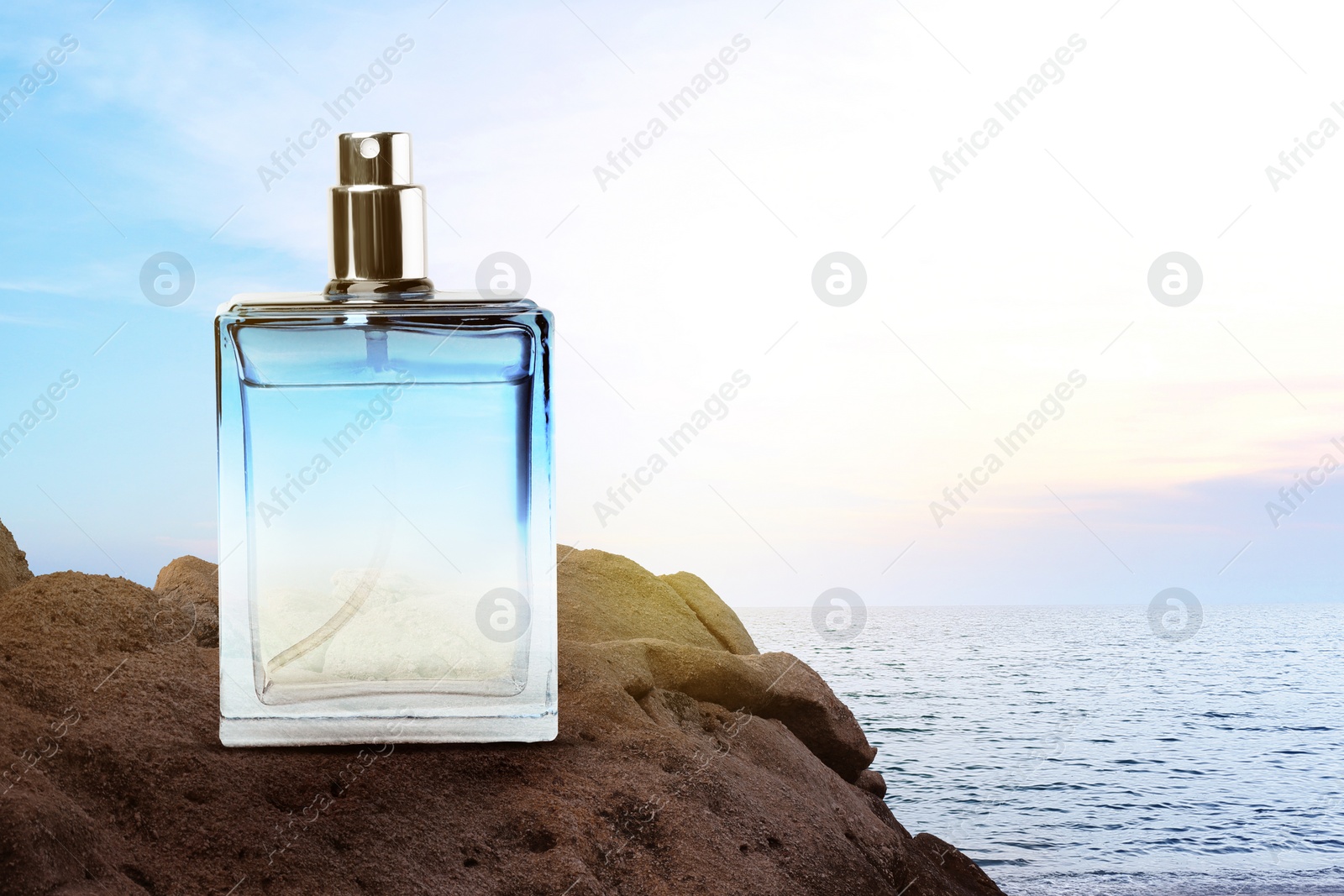 Image of Bottle of aquatic perfume on rock near ocean. Fresh sea breeze scent