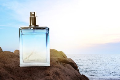 Image of Bottle of aquatic perfume on rock near ocean. Fresh sea breeze scent