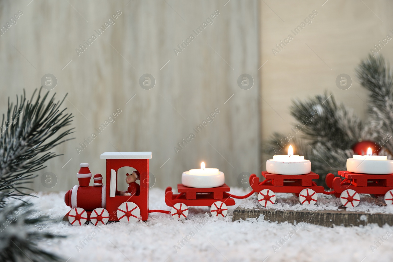 Photo of Red toy train as Christmas candle holder on table with artificial snow in room