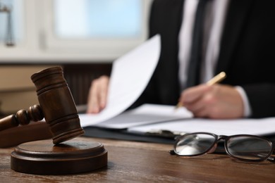 Photo of Lawyer working with documents at wooden table in office, focus on gavel