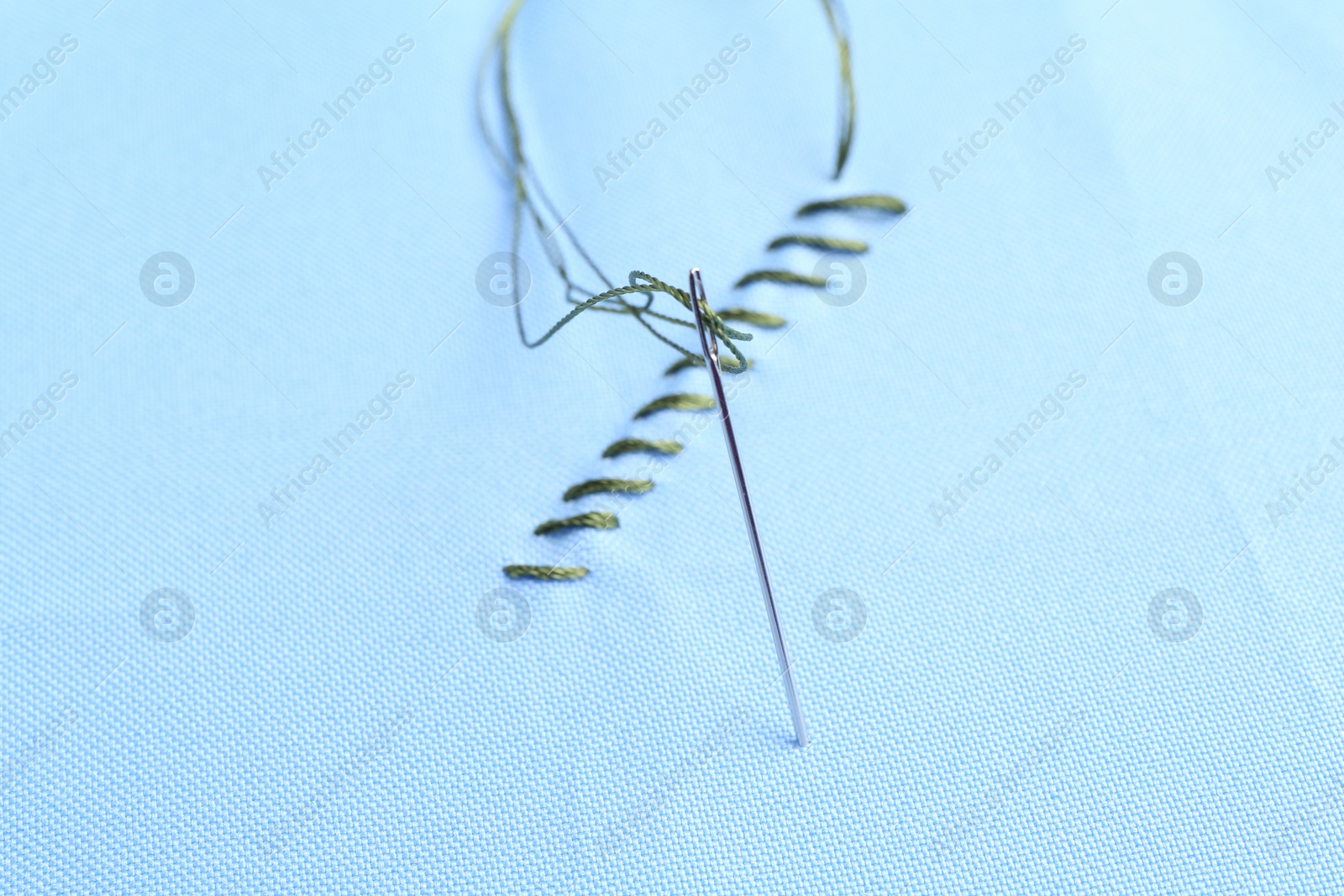 Photo of Sewing needle with thread and stitches on light blue cloth, closeup