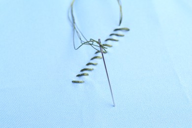 Photo of Sewing needle with thread and stitches on light blue cloth, closeup