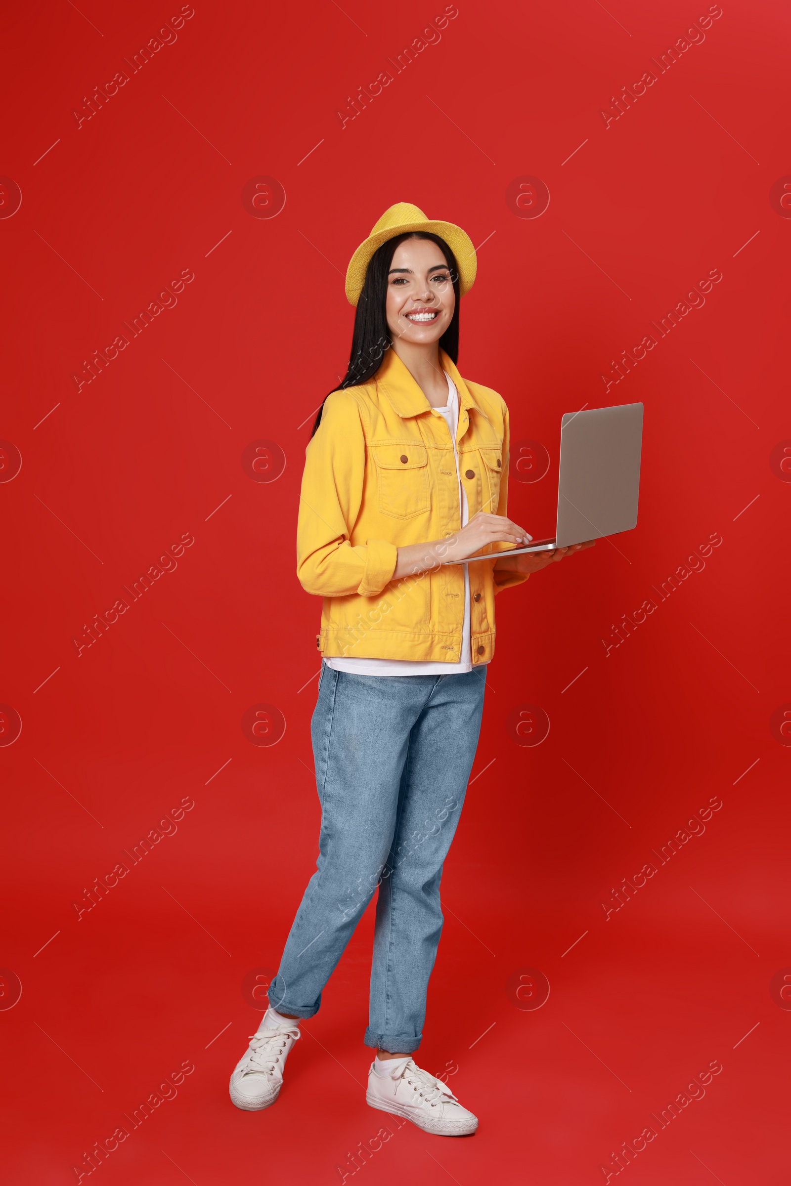 Photo of Young woman with modern laptop walking on red background