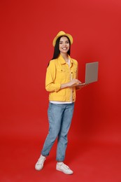 Young woman with modern laptop walking on red background