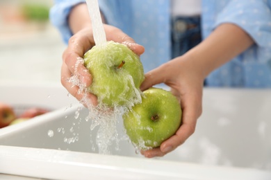 Photo of Woman washing fresh green apples in kitchen sink, closeup