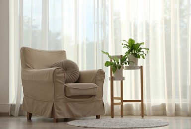 Comfortable armchair and beautiful plants near window indoors