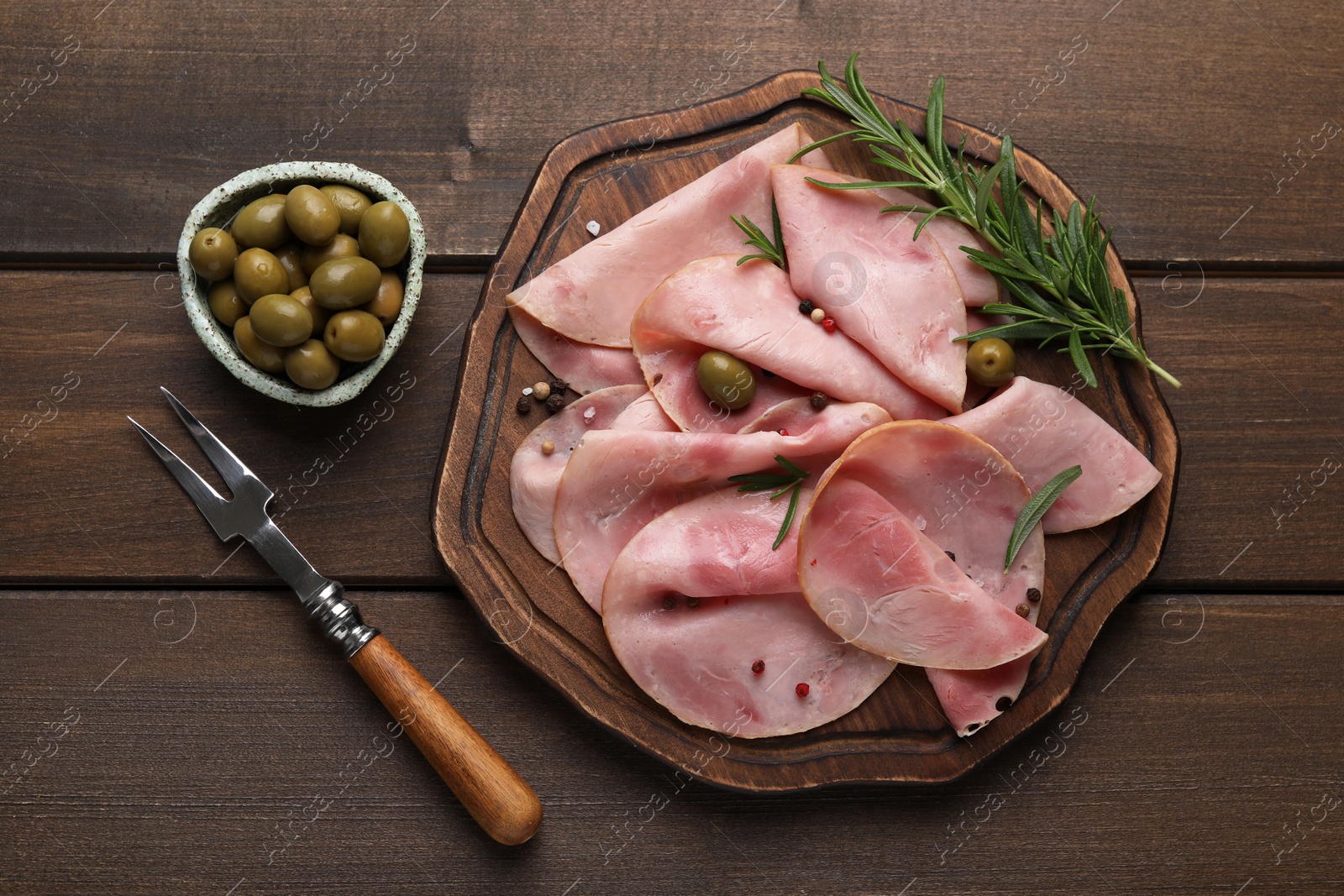 Photo of Slices of delicious ham with rosemary and olives served on wooden table, flat lay