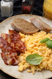 Delicious scrambled eggs with bacon and products on wooden table