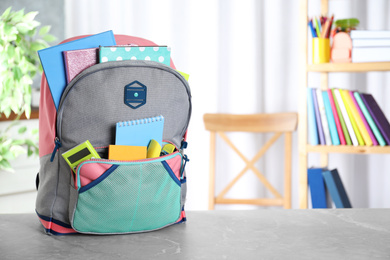 Photo of Stylish backpack with different school stationery on table indoors. Space for text