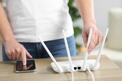 Woman with smartphone connecting to internet via Wi-Fi router at table indoors, closeup