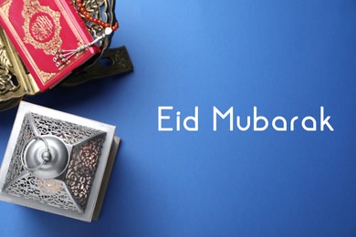 Image of Eid Mubarak greeting card. Arabic lantern, Quran and misbaha on blue background, flat lay