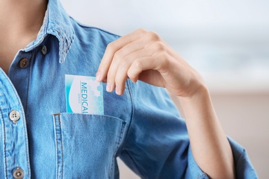 Photo of Woman putting business card into pocket on blurred background, closeup. Medical service